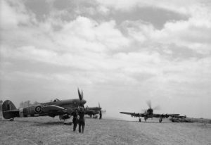 198 Sqn. Typhoons on airfield B10/Plumetot, France, in July 1944. MN526 TP-V has the larger Tempest tailplane and a four-bladed propeller. A heavy dust cloud has been stirred up by the taxiing aircraft.