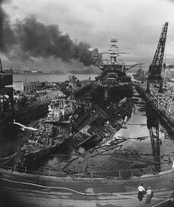 The wrecked destroyers USS Downes (DD-375) and USS Cassin (DD-372) in Drydock One at the Pearl Harbor Navy Yard, soon after the end of the Japanese air attack. Cassin has capsized against Downes. USS Pennsylvania (BB-38) is astern, occupying the rest of the drydock. The torpedo-damaged cruiser USS Helena (CL-50) is in the right distance, beyond the crane. Visible in the center distance is the capsized USS Oklahoma (BB-37), with USS Maryland (BB-46) alongside. The smoke is from the sunken and burning USS Arizona (BB-39), out of view behind Pennsylvania. USS California (BB-44) is partially visible at the extreme left. Date 7 December 1941