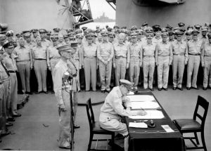 : General Douglas MacArthur signs as Supreme Allied Commander during formal surrender ceremonies on the USS MISSOURI in Tokyo Bay. Behind General MacArthur are Lieutenant General Jonathan Wainwright and Lieutenant General A. E. Percival. Date 2 September 1945